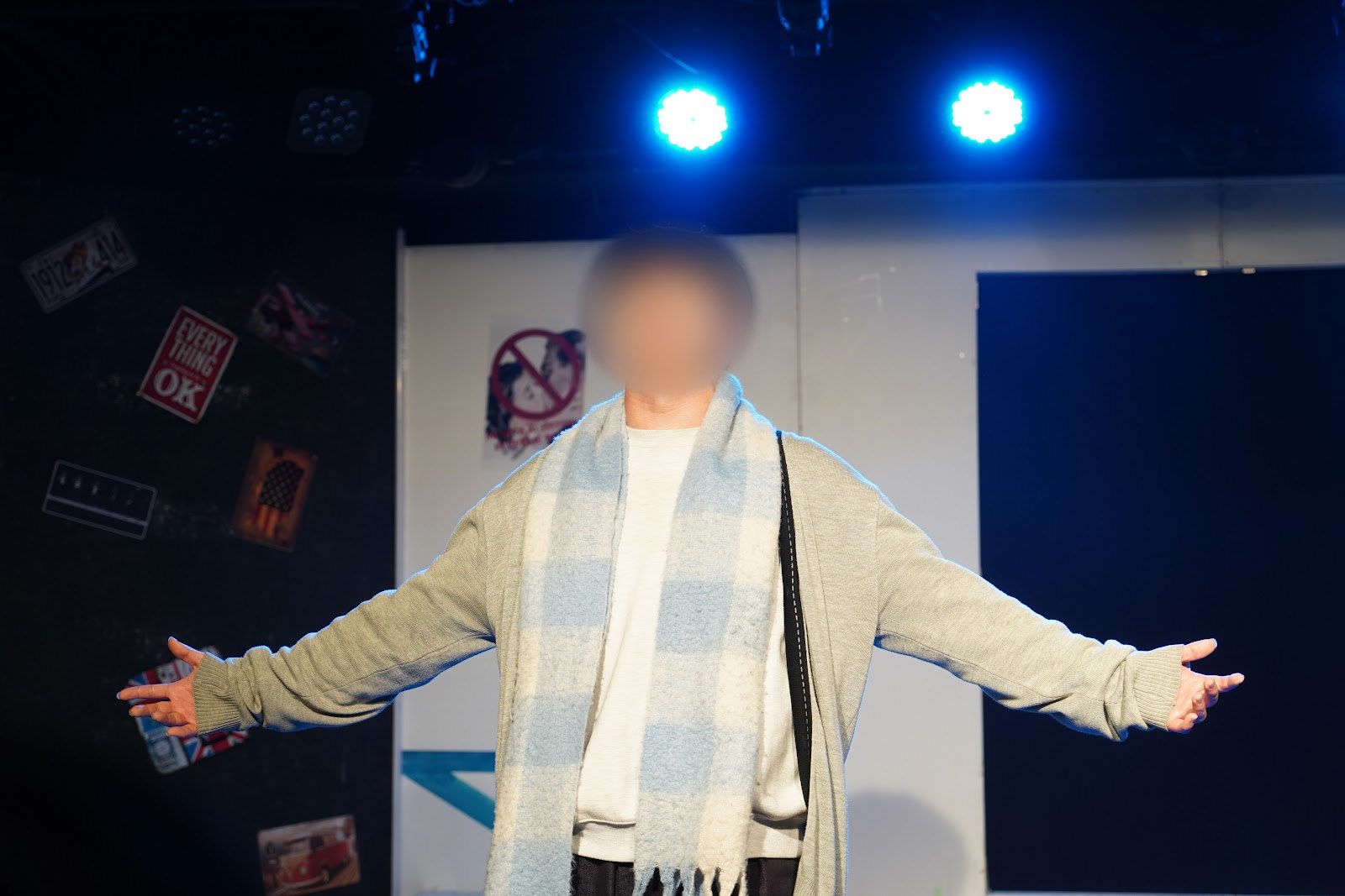 파란 조명 아래 목도리를 두른 배우가 두 팔을 활짝 펴고 노래하는 장면입니다.