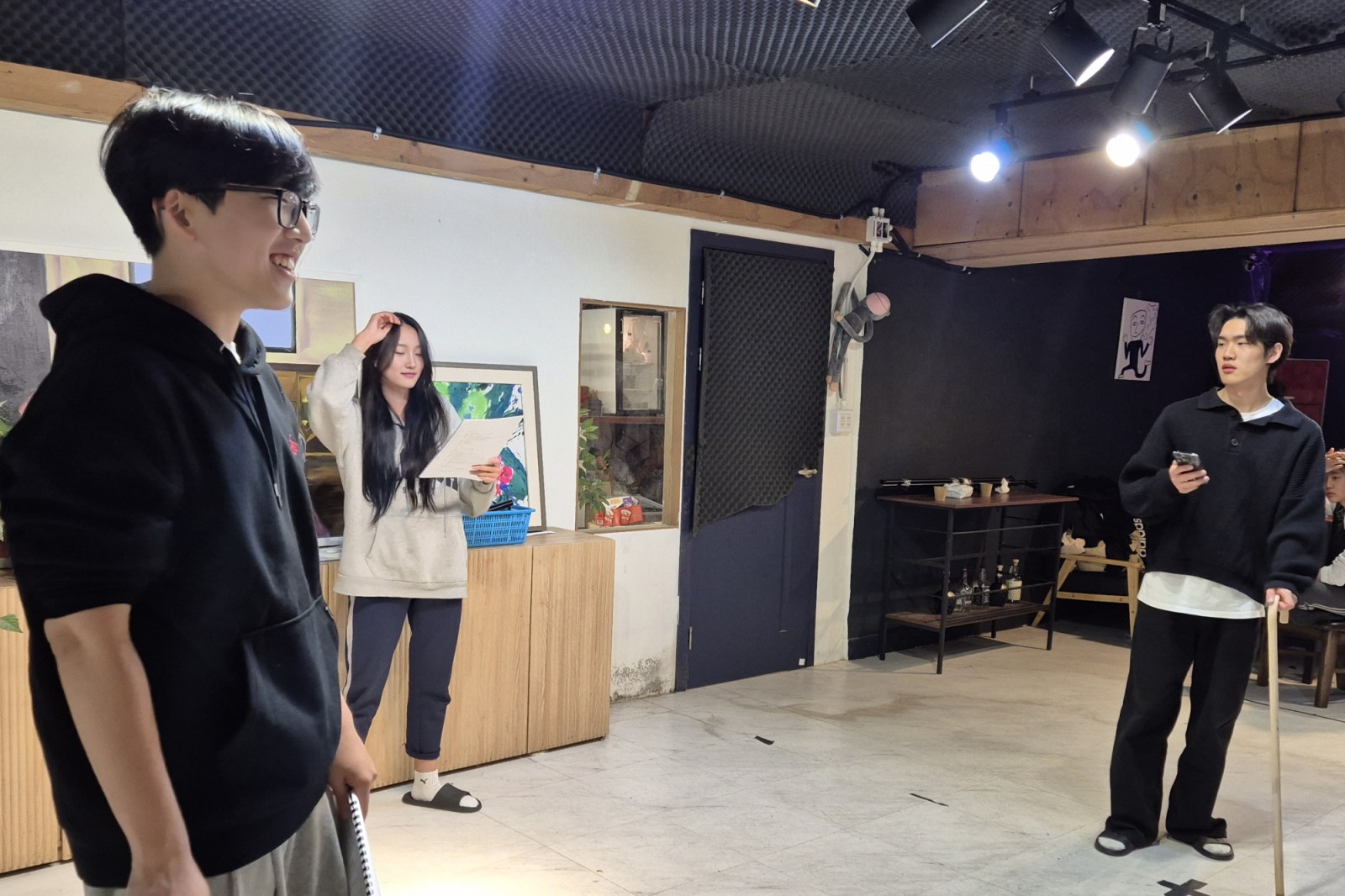연습실에서 단원들이 대본을 들고 웃으며 이야기하는 모습입니다.